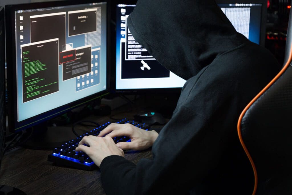 A cybercriminal in a dark hoodie uploads malicious code onto a server to cause trouble.