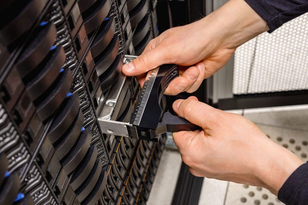 IT professional replacing a disk drive in a server at a datacenter.